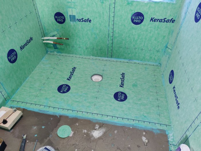 Golv under renovering med vattentätning och avlopp i centrum, verktyg och lim syns.