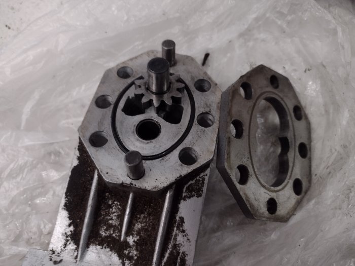 Demonterad hydraulpump i två delar på en plastpåse, tecken på slitage och potentiell skada.