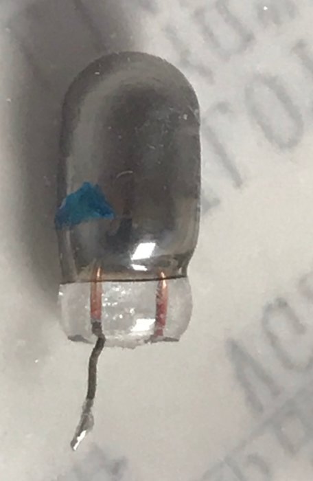 Närbild på en gammal elektronisk komponent, möjligen en lampa, med två anslutna ledningar.