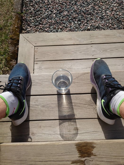 Person sitter på trätrall med en vattenglas mellan fötterna i sommarväder.