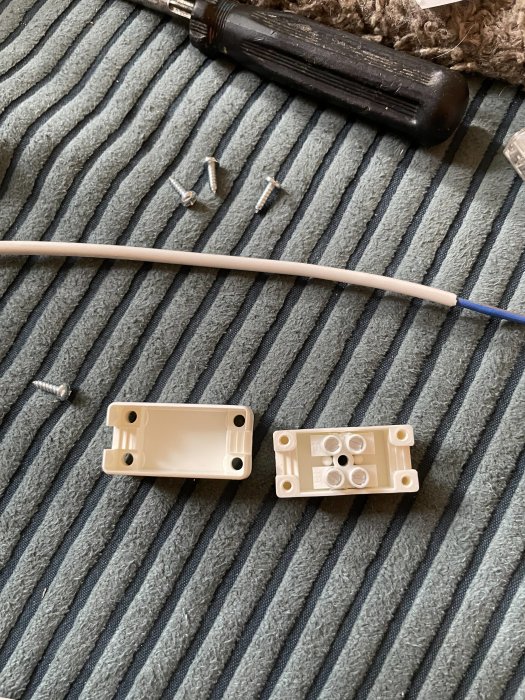 Eluttagets bakstycken på grå matta med skruvar och en del av en skruvmejsel och kabel.