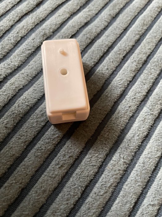 En beige strömbrytare ligger på ett grått randigt tyg.