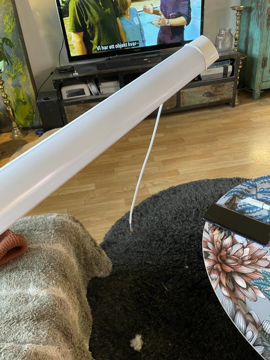 Vardagsrum med utrullad vit byggplast, TV i bakgrunden, och en mönstrad bricka på matta.