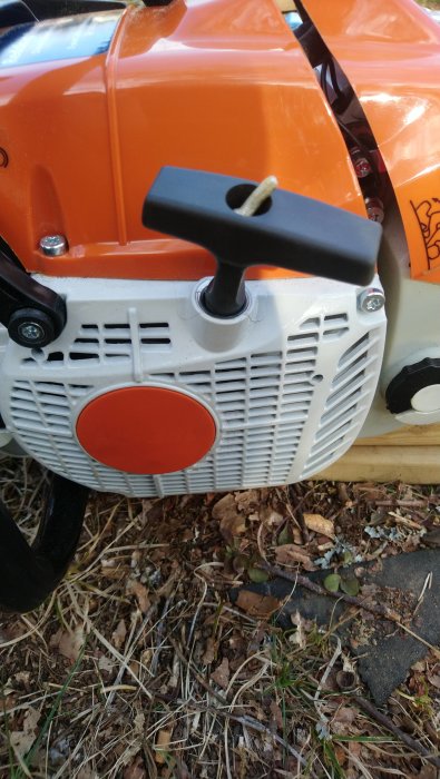 Motorsågens startmekanism och luftfilterhus, delvis skymd Stihl-logotyp.