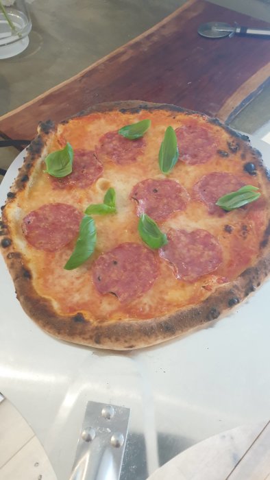 Nybakad pizza med pepperoni och färska basilikablad på en träskärbräda.