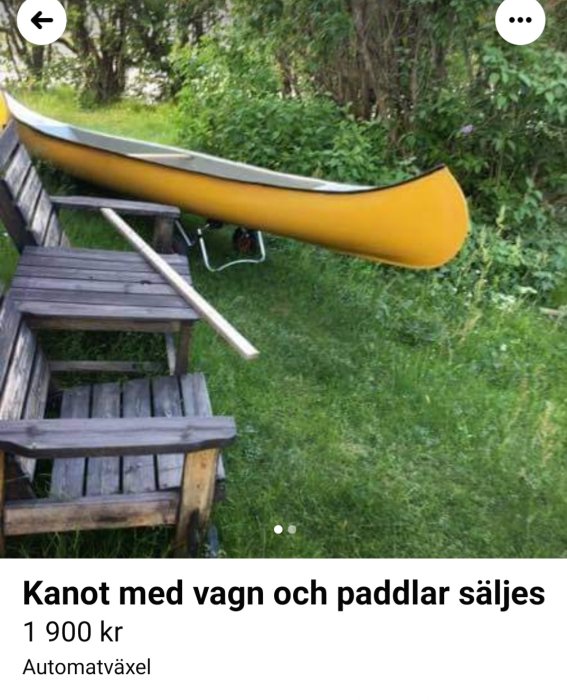 Gul kanot uppställd på gräs bredvid en träbänk, till salu.