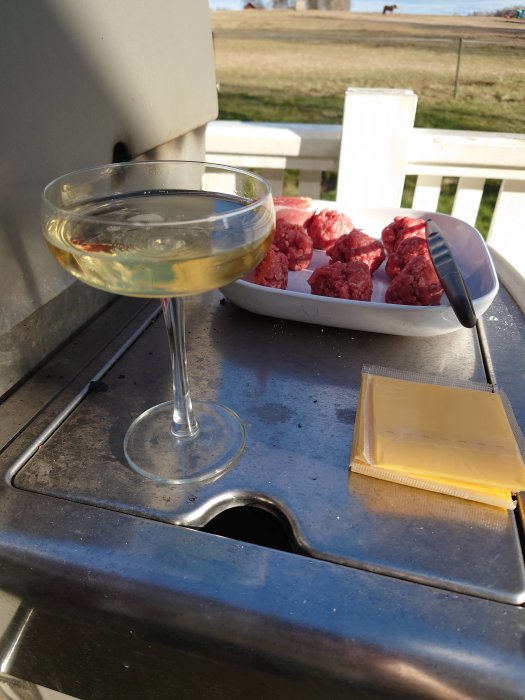 Glas med champagne bredvid råa smashburgare på en bricka utomhus vid en grill.