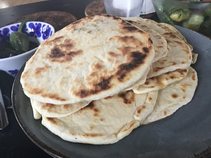 Nybakade hemgjorda stekpannebröd staplade på mörk tallrik med bruna fläckar från grillning.