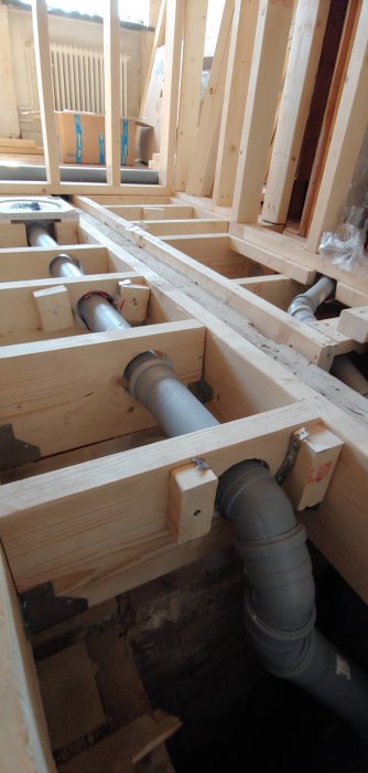 Nydragna avloppsrör fastsatta med hålband mellan träbjälkar under badrumsrenovering.