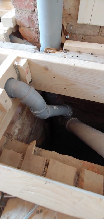 Avloppsrör installation i pågående badrumsbygge, synligt med hålband och träbjälkar.