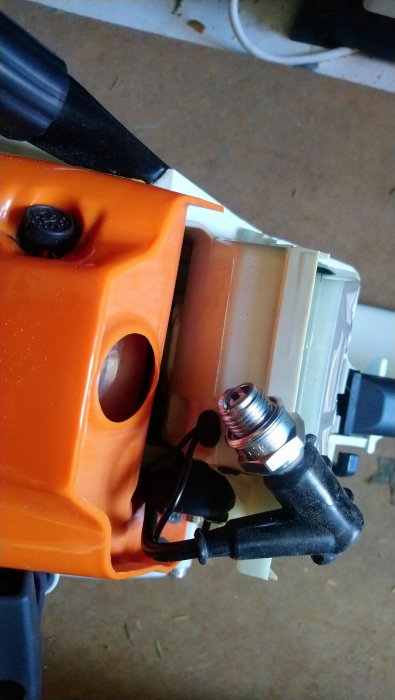 Närbild på ett tändstift kopplat till en motor, med fokus på stiftets anslutning och det intilliggande området.