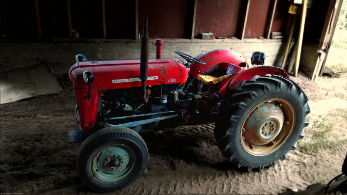 En röd Massey Ferguson 35 traktor parkerad i ett mörkt lada.