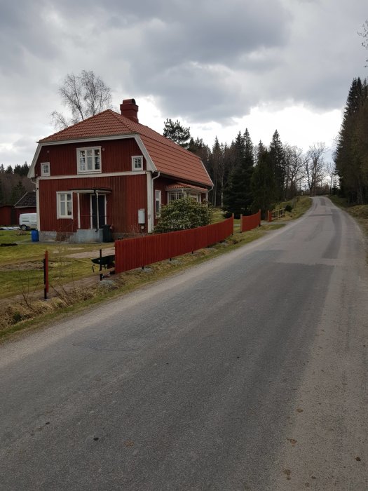 Rött hus vid landsväg med nybyggt staket och nyplanterad slänt vid infart.