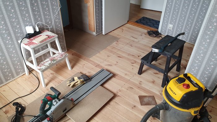 Rum under renovering med en sänksåg, skivor av trämaterial, och en dammsugare på golvet.