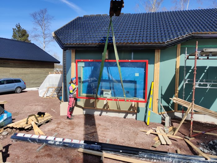 Person monterar ett stort fönster i en byggnads fasad med hjälp av ett lyftredskap.