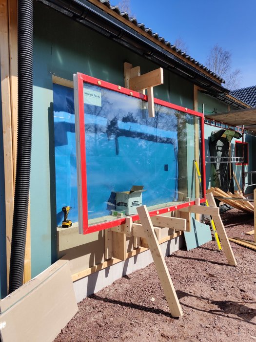 Stort fönster monterat på provisoriskt stativ under installation vid husbygge.