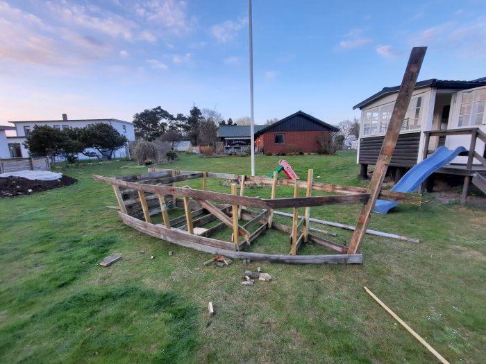 Påbörjat bygge av en lekbåt utomhus med återanvända trallbrädor från en badbrygga, verktyg och brädor på gräset.