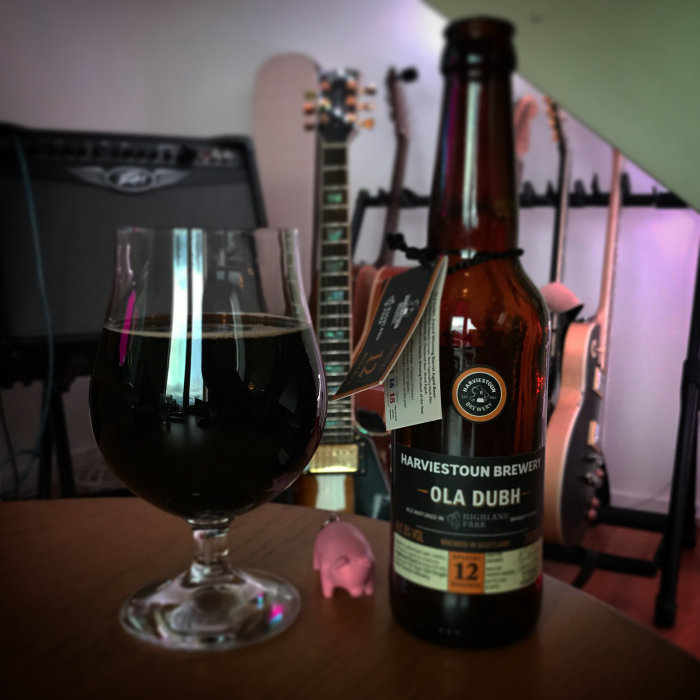 Mörk stout i glas med flaska whiskyfatslagrad öl framför elgitarrer.