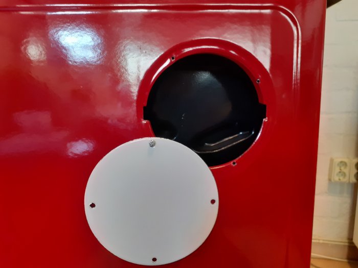 Vitt lock monterat på sidoutgång av en röd spispanna, tänkt att förslutas.