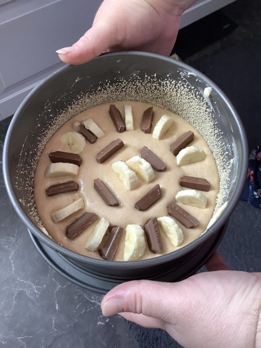 Oformad choklad- och banankaka i springform med bitar av choklad och bananskivor fördelade över smeten.
