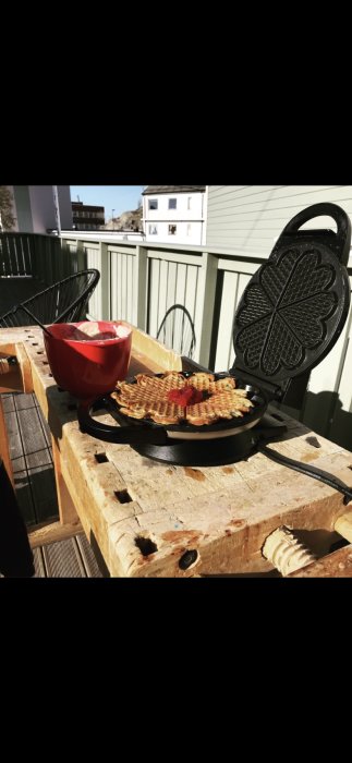 Gammal snickarbänk utomhus används för att laga våfflor med en gjutjärnsvåffeljärn på en solig altan.