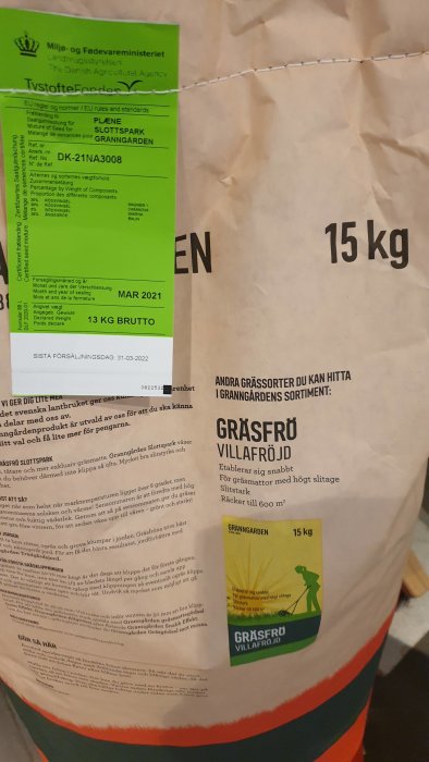 Påse med gräsfrö märkt "15 kg", faktisk vikt angiven som "13 KG BRUTTO", närbild på etiketter.