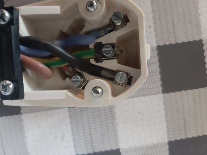Elektrisk anslutning av en spis med tre kablar: en blå, en brun och en gulgrön, emot en vit plastanslutning.