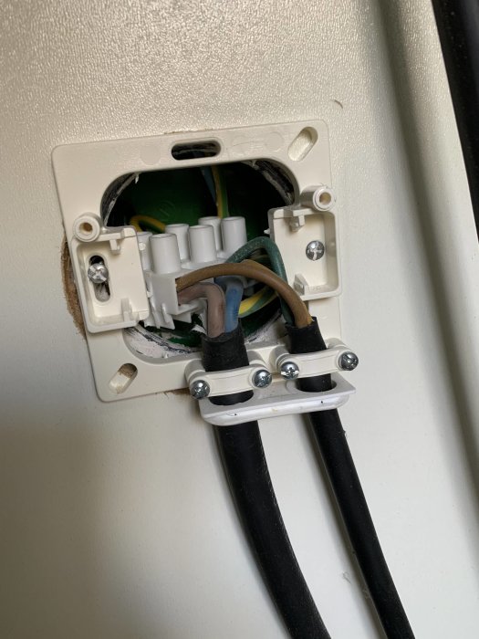 Öppet eluttag med en gul/grön, blå och brun kabel kopplade, samt två svarta kablar i sockerbit.