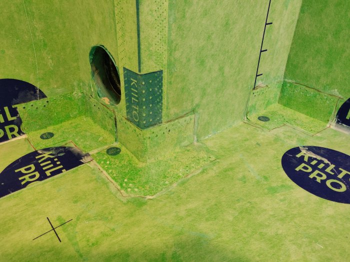 Grönt tätskikt med installerade brunnsmanschetter, klart för kakelarbete i ett badrumsrenoveringsprojekt.