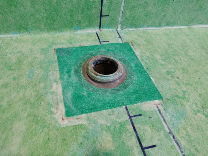 Golv med nylagt tätskikt runt ett avloppsrör, markerade linjer och brunnsmanschett.