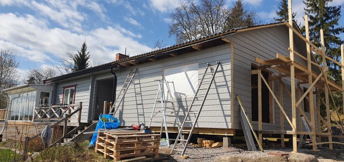 Hus under renovering med OSB som ytterväggar, luftspalt, provisoriska knutbrädor och byggmaterial framför.