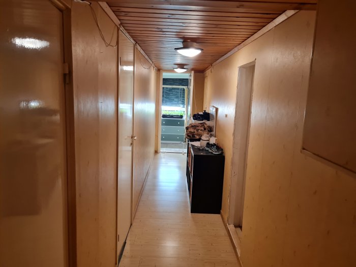 Husets källargång med laminatgolv, trätak, och ljusa väggar, visande renoveringsförberedelser.