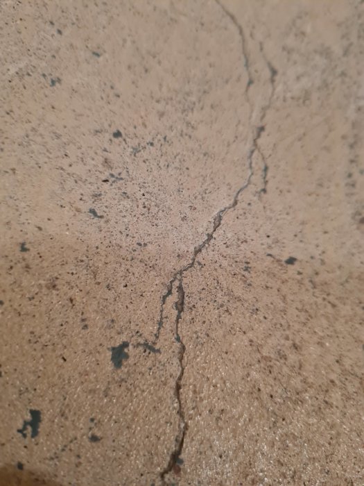 Närbild på betonggolv med en spricka och flagnande färg, tecken på tidigare renovering i en källare.