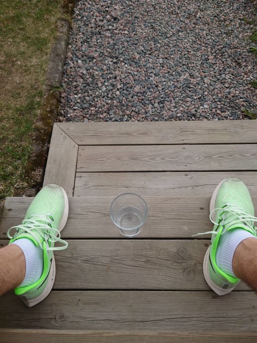 Person med ljusgröna sportskor sitter på en trätrall vid kanten mot en grusgång, med en tom glaskopp framför sig.
