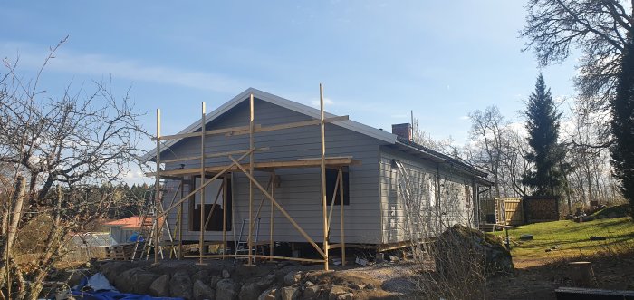 Hus under renovering med ny vindskiva och fasadbeklädnad, stöttat av byggnadsställningar.