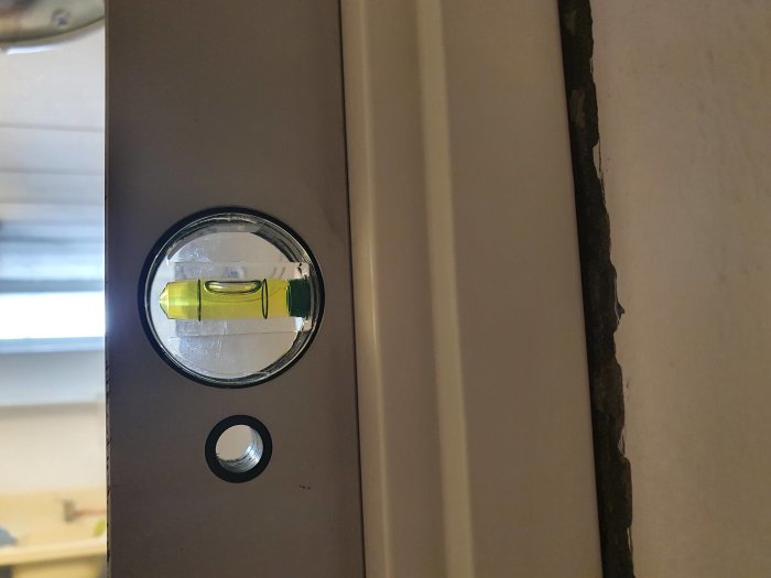 Nivåbubbla på en dörrkarm visar att karmen inte är lodrät medan dörren hänger och eroderad kant syns.