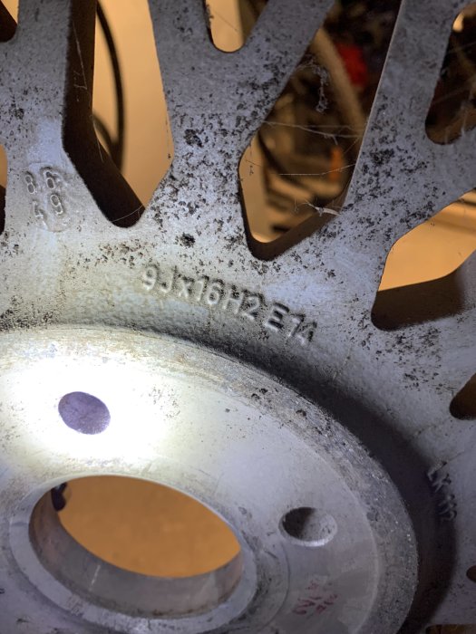 Närbild på bilmärkning "9JX16H2 ET34" på en däckfälg, med smuts och spindelnät.