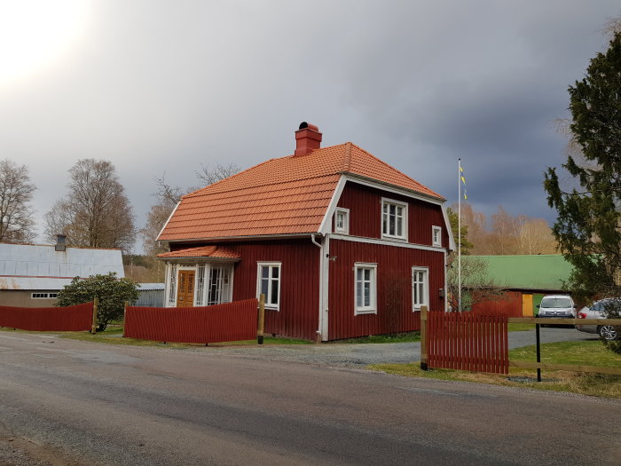 Ett rött hus med tegeltak och rött staket, infarten framför huset syns.