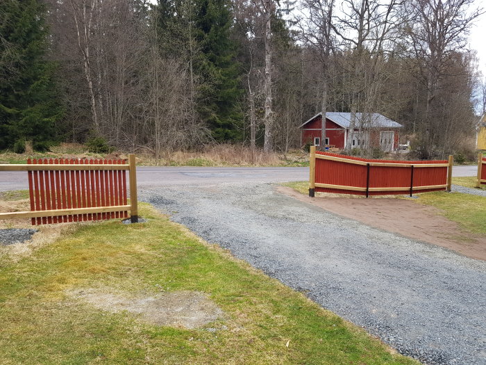 Nyligen riktad infart med grus och en mindre lutning, gräsområde och en röd trästaket vid sidan av en landsväg.