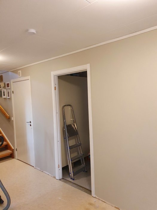 Nymålat rum med öppen dörr, stege inuti och tejpade dörrkarmar.
