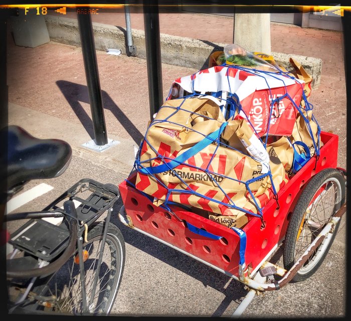 Lastcykel med en röd lastkorg full av hopvikta papperskassar säkrade med nät.