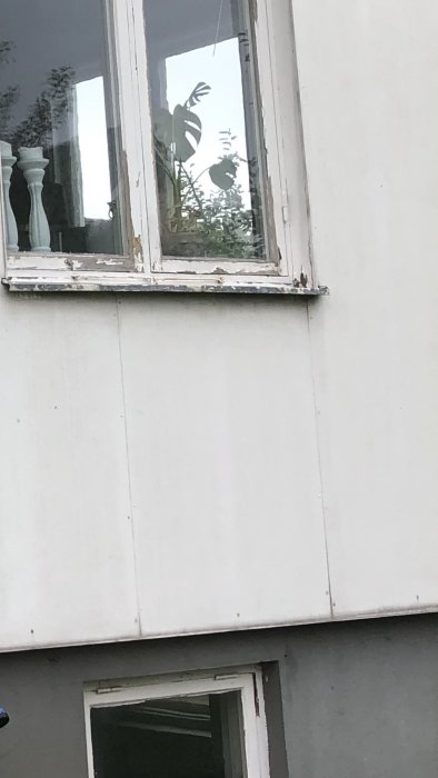 Fasaddetalj av ett hus med slitna fönsterkarmar och vita skivor, eventuellt eternitskivor, från 60-talet.