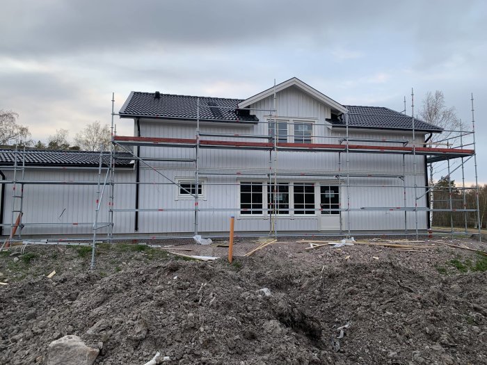 Nybyggt hus med ställningar runtom, rör och slangar på marken framför huset.