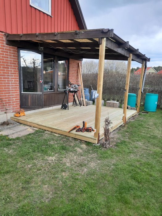 Nybyggd trädäck vid röd tegelvilla med verktyg och minimalt spill.