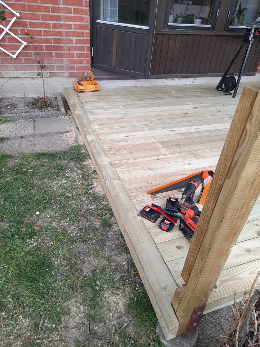 Nylagd trädgårdstrall vid röd tegelvägg, med verktyg och minimalt spill synligt.