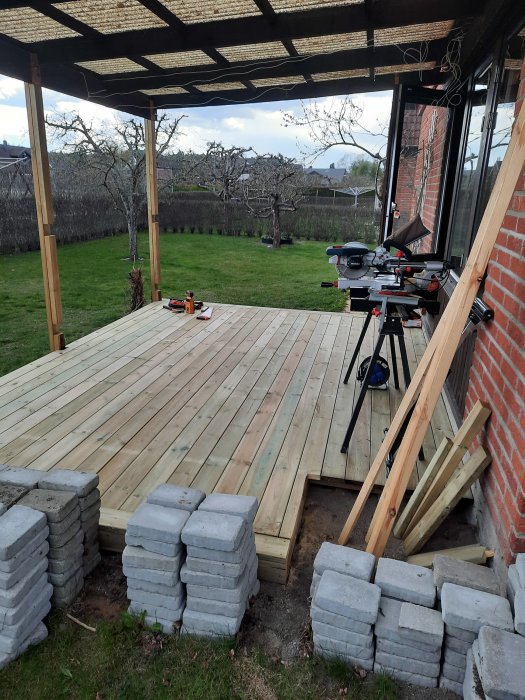 Nybyggd trätrall vid ett hus med verktyg och minimalt spillmaterial, omgiven av en trädgård.