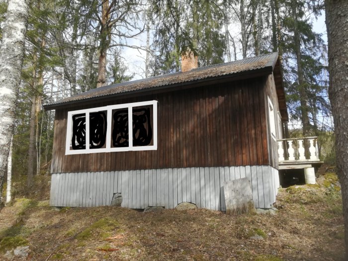 En sommarstuga med överskaligt ritade fönstermarkerade för byte, belägen i en skogsmiljö.