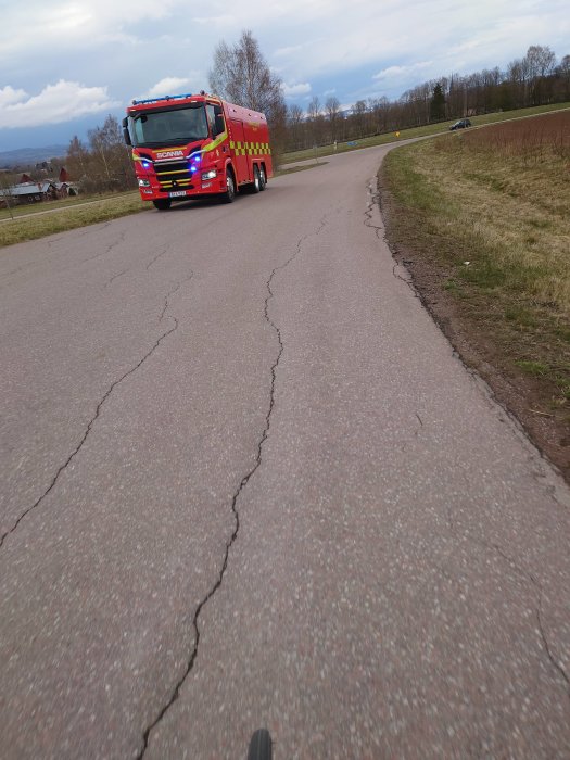 En färgglad brandbil kör på en asfalterad väg med sprickor under en molnig himmel.