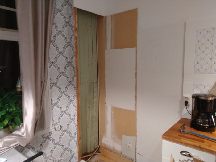 Renovering av kök med partiellt avlägsnad vägg som avslöjar äldre grönmålad pärlspontspanel, omgiven av tapet och kakel.