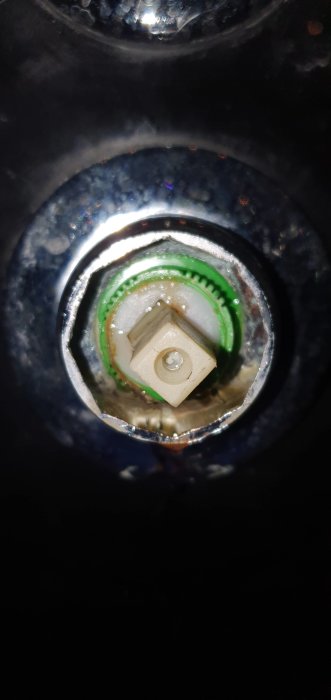 Närbild på en läckande duschblandarens patron i plast, synlig inuti monteringsöppningen.